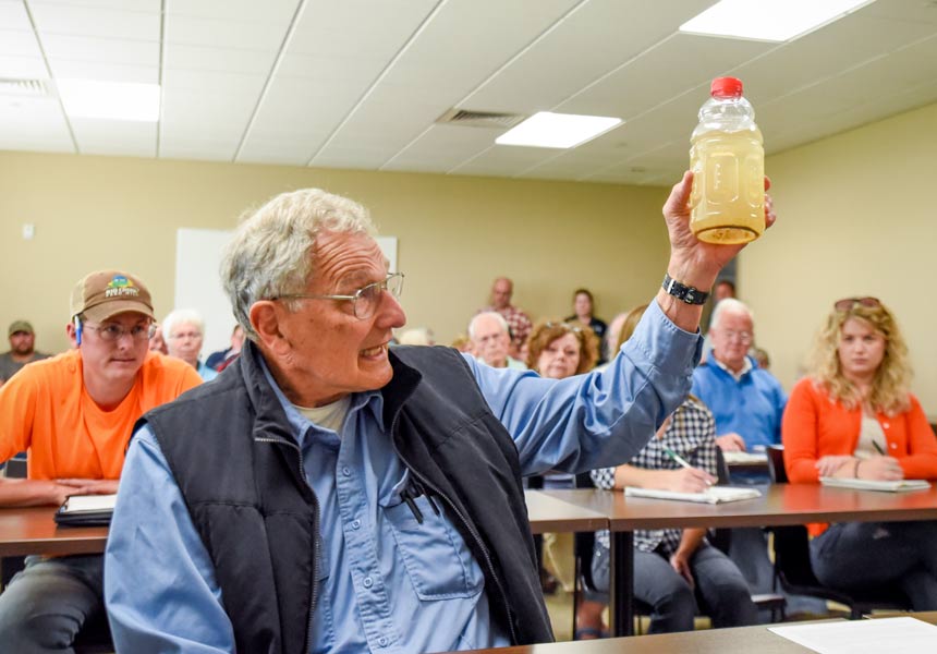 William Faller holds up a water sample from a local creek containing an overabundance of silt, bacteria and nutrients during a water quality hearing in Kewaunee County on June 27. (Photo by Mike Peters)